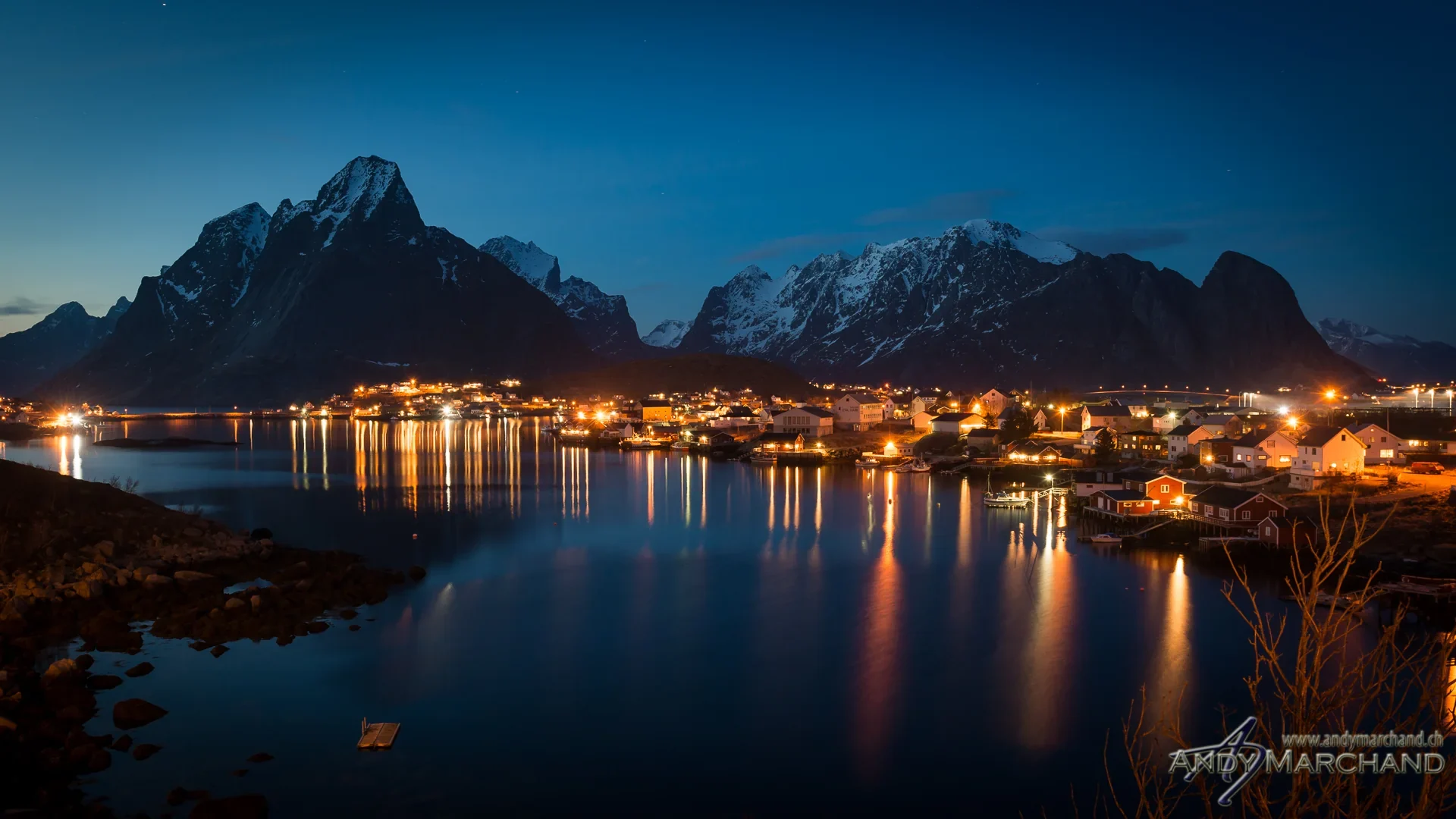 Beleuchtetes Küstendorf und Berge während der blauen Stunde auf den Lofoten