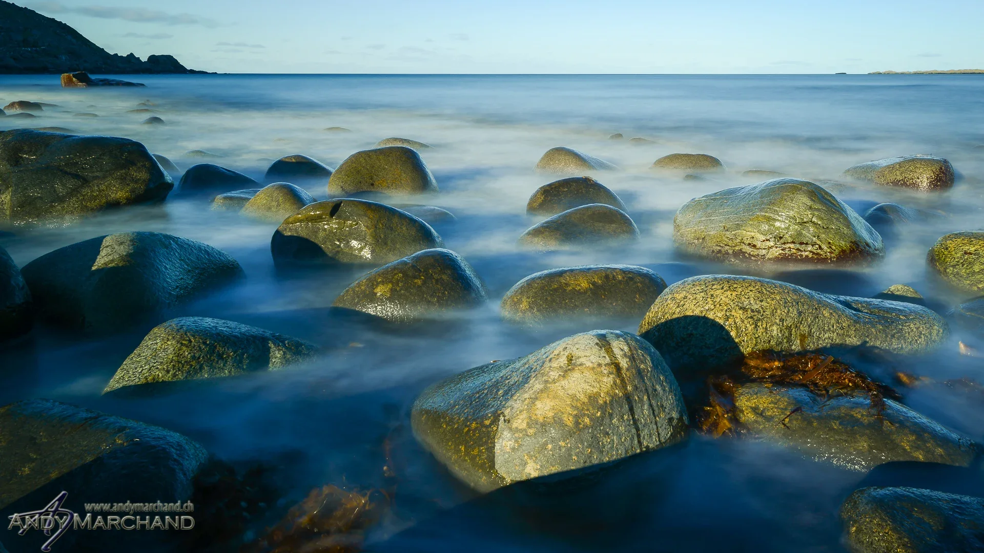 Rundgeschliffene Steine im weich fliessenden blauen Wasser an der Küste der Lofoten